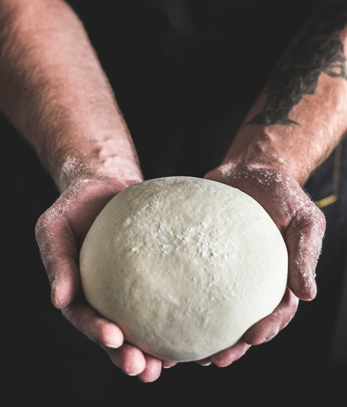 Les mains du pizzaïolo présentant un pâton de pâte à pizza