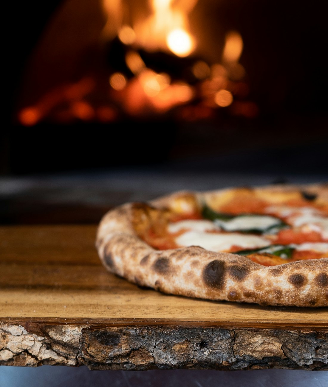 Pizza margherita napolitaine, bords gonflés et légèrement grillés, posée sur une planche en bois